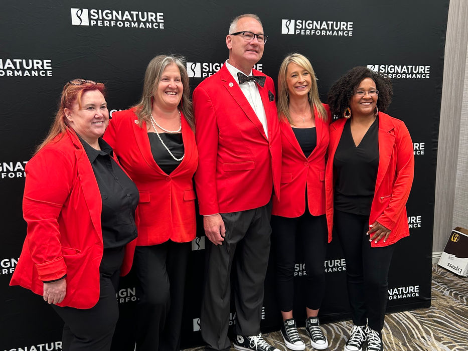 Signature Performance team posing in red attire at a company event